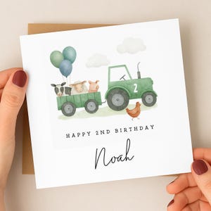 May include: A square greeting card featuring a watercolor illustration of a green tractor with the number 2, pulling a trailer filled with a cow, sheep, and pig. Three balloons float above, and a chicken stands nearby. Text reads HAPPY 2ND BIRTHDAY Noah.