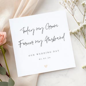 Op de afbeelding: Een witte trouwkaart met zwarte tekst: "Today my Groom, Forever my Husband." De kaart bevat ook "Our Wedding Day" en de datum 01.01.26. Onderaan staat een klein gouden hartje. De kaart is omringd door bloemen.