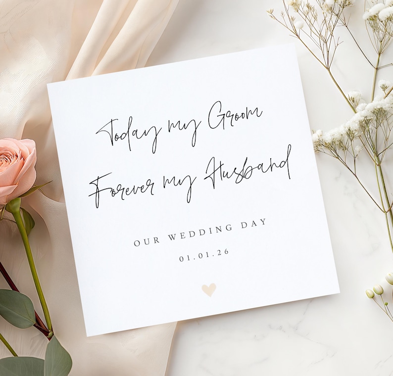 Op de afbeelding: Een witte trouwkaart met zwarte tekst: "Today my Groom, Forever my Husband." De kaart bevat ook "Our Wedding Day" en de datum 01.01.26. Onderaan staat een klein gouden hartje. De kaart is omringd door bloemen.
