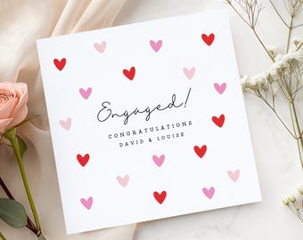May include: White engagement card with red and pink hearts scattered across the surface. The card reads "Engaged!" in elegant script, with "Congratulations David & Louise" below.