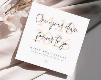 May include: A square, cream-coloured anniversary card with black script that reads "One year down, forever to go." The numbers "2023" are in a light tan colour. The card also says "Happy Anniversary to my wonderful husband."