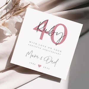 May include: A white card with the text "Ruby 40" in pink and black script. The card reads "With love on your fortieth anniversary" and "Mum & Dad" with the years 1986 and 2026.