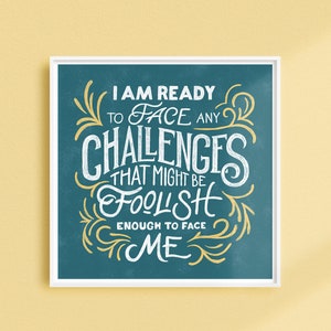 May include: Square framed art print with the quote "I AM READY TO FACE ANY CHALLENGES THAT MIGHT BE FOOLISH ENOUGH TO FACE ME" in white and yellow script on a teal background. The print is displayed on a yellow wall.