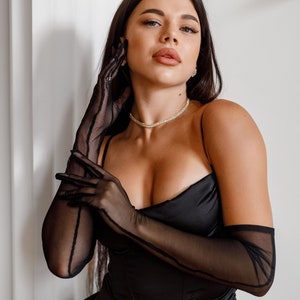 May include: A person wearing a black satin dress with a plunging neckline and long black mesh gloves.