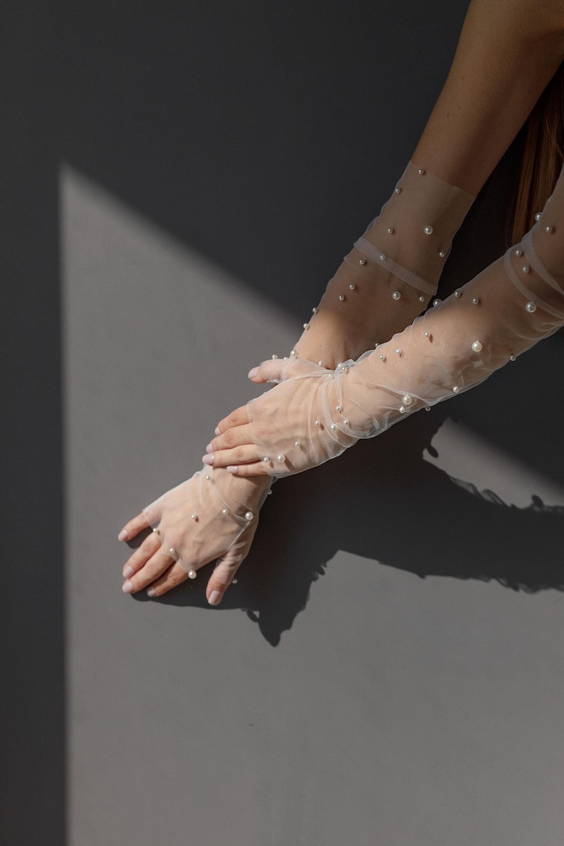 May include: A pair of sheer white gloves with pearl embellishments. The gloves are on a gray background.