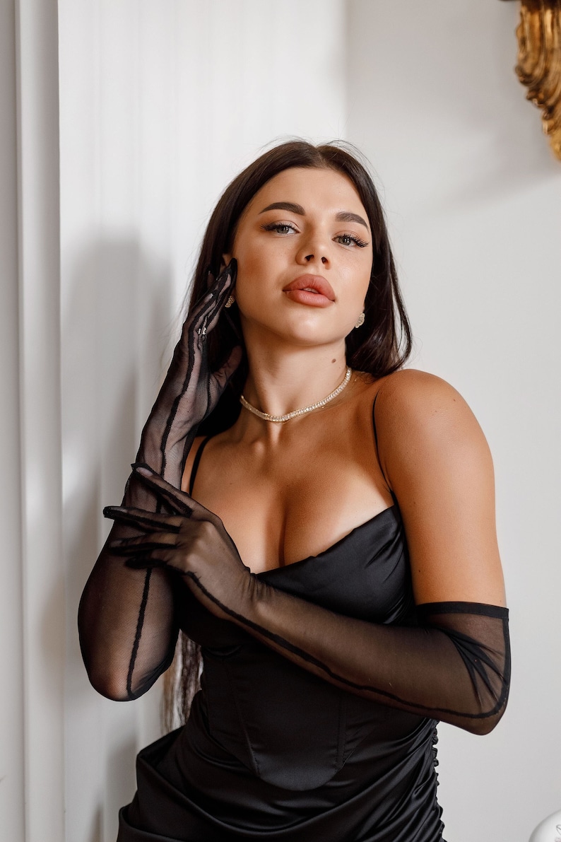 May include: A person wearing a black satin dress with a plunging neckline and long black mesh gloves.