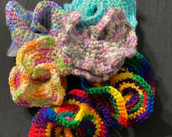 May include: A collection of colorful crocheted flowers in shades of blue, pink, purple, green, yellow, and red. The flowers are made with different stitch patterns and textures.
