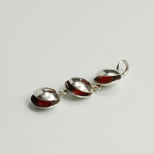 May include: A silver-toned pendant necklace featuring three circular charms. Each charm has a silver top and a red, rounded interior. The charms are connected by small silver links, and the pendant has a small loop at the end.