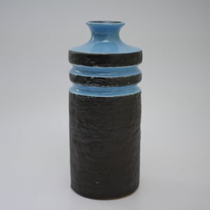 May include: A ceramic vase with a textured black base and a light blue top. The vase has two black bands around the middle and a narrow neck. The vase is approximately 25 cm tall.