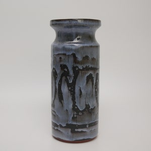 May include: A cylindrical ceramic vase featuring a glossy glaze with a drip pattern in shades of light blue, grey, and deep black. The vase has a flared rim and a straight body, showcasing a layered, textured finish that transitions from dark tones at the base to lighter hues near the top opening.