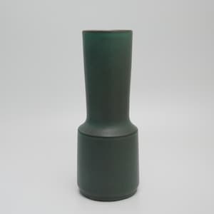 May include: A dark green ceramic vase with a cylindrical design. The vase features a wider base that narrows towards the neck and a slightly flared rim. The dark green colour gives it a modern, minimalist aesthetic. Suitable for displaying flowers or as a decorative item.