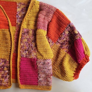 Op de afbeelding: Een gebreid vest met een patchwork-ontwerp in tinten roze, oranje en geel. Het vest heeft een losse pasvorm en een lange, open voorkant.