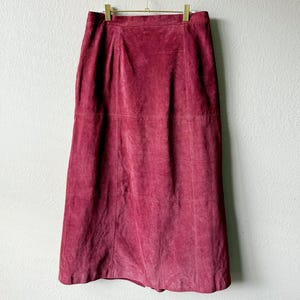 May include: A deep burgundy suede midi skirt featuring a high-waisted design with a structured waistband and visible vertical and horizontal seam detailing throughout the garment, creating a paneled appearance that extends to the hemline.