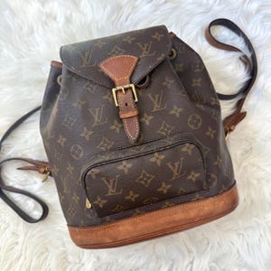 Puede incluir: Mochila marrón con monograma, bolsillo delantero y detalles en cuero. La mochila tiene un cierre de solapa con hebilla y correas ajustables. La bolsa tiene una base de cuero marrón y está hecha de un material duradero.