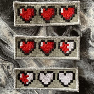 May include: Three rows of pixelated heart patches. The top row has three full red hearts. The middle row has two full red hearts and one half-full red heart. The bottom row has one half-full red heart and two full white hearts.