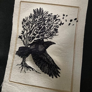 Puede incluir: Parche bordado que representa un cuervo negro en vuelo, llevando un árbol con raíces. El cuervo se encuentra sobre un fondo crema con un borde cosido. El diseño incluye hojas cayendo, creando un tema inspirado en la naturaleza.