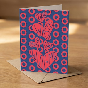 May include: A greeting card with a blue background and red circles. The card features red hearts with the words "Come Waste Your Time With Me" in a handwritten style. The card is on a brown envelope.