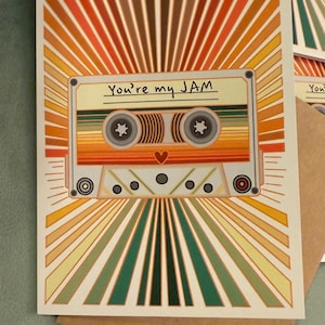May include: Greeting card with a retro cassette tape design. The card features a colorful striped cassette tape with the text "You're my JAM". The background has a sunburst design in shades of orange, yellow, and green.