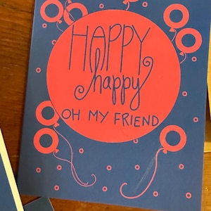 May include: A blue card with a red circle and the text "Happy Happy Oh My Friend" in black. The circle is surrounded by pink balloons.