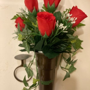 May include: A bouquet of red roses with green leaves in a brown ceramic vase. The vase is attached to a wall mount.