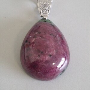 May include: A teardrop-shaped pendant with a pink and green gemstone set in a silver filigree bail.