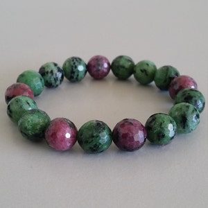 May include: A green and pink gemstone bracelet with faceted beads. The bracelet is made of natural stones and is approximately 18 cm in length.