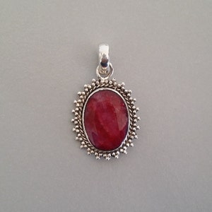 May include: A silver pendant featuring a red oval gemstone set in a decorative silver frame.