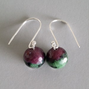May include: A pair of silver earrings with green and purple gemstone drops.