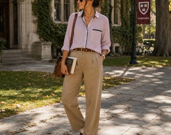 May include: A long-sleeved button-down shirt with vertical red and white stripes, featuring a dark trim on the chest pocket. The shirt is paired with high-waisted khaki trousers with front pleats, a brown leather belt, and brown leather loafers.