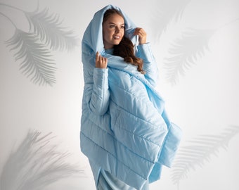May include: A light blue quilted jacket with a hood. The jacket is worn over a matching light blue maxi dress. The model is standing on a white background.
