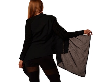 May include: A woman wearing a black long-sleeved top with a long, flowing black scarf. The top has a zip down the front and the scarf is draped over one shoulder.