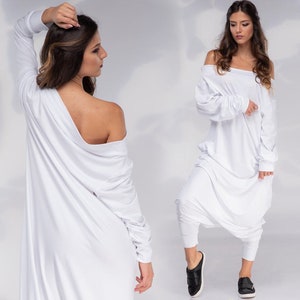 May include: A white off-the-shoulder jumpsuit with long sleeves and a loose fit. The jumpsuit has a gathered detail at the waist and a wide leg.