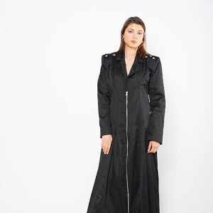 May include: A long black coat with a zipper closure and a stand-up collar. The coat has a slightly flared silhouette and features decorative accents on the shoulders.