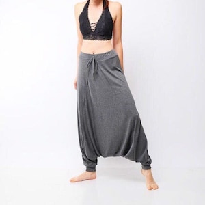 May include: A woman wearing a gray pair of loose-fitting pants with a drawstring waist and a black lace halter top.