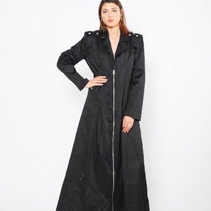 May include: A long black coat with a zipper closure and a stand-up collar. The coat has a slightly flared silhouette and is made of a smooth, lightweight fabric.