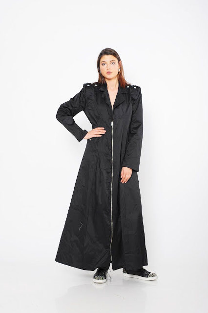 May include: A long black coat with a zipper closure and a stand-up collar. The coat has a slightly flared silhouette and is made of a smooth, lightweight fabric.