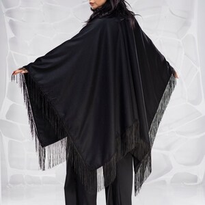 Puede incluir: Un poncho negro con flecos y un dise&ntilde;o largo y fluido. El poncho est&aacute; hecho de una tela suave y ligera y tiene un corte holgado.