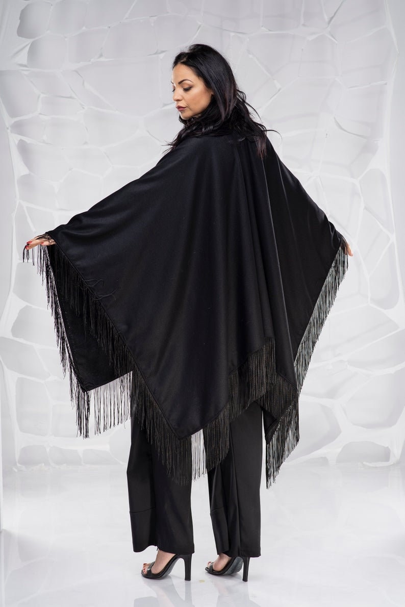 Puede incluir: Un poncho negro con flecos y un dise&ntilde;o largo y fluido. El poncho est&aacute; hecho de una tela suave y ligera y tiene un corte holgado.