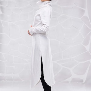 May include: A white long-sleeved tunic with a high collar and a side slit. The tunic is made of a lightweight fabric and has a relaxed fit.