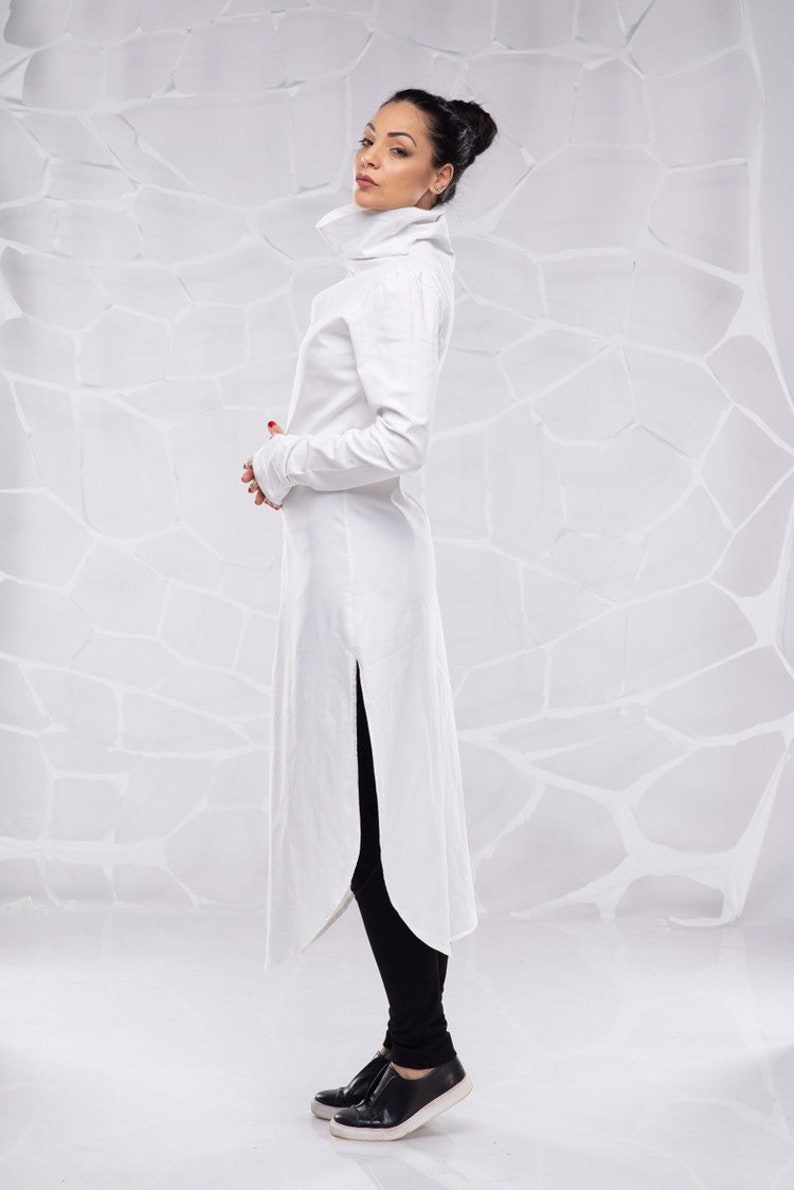 May include: A white long-sleeved tunic with a high collar and a side slit. The tunic is made of a lightweight fabric and has a relaxed fit.