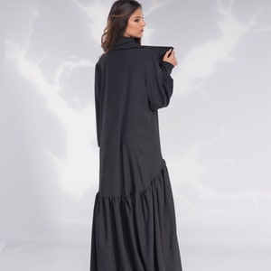 May include: A black long-sleeved dress with a ruffled hem. The dress has a high collar and a relaxed fit.