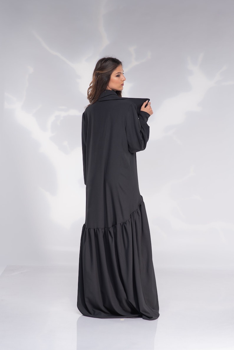 May include: A black long-sleeved dress with a ruffled hem. The dress has a high collar and a relaxed fit.