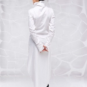 May include: A white long-sleeved shirt with a high collar and a long, flowing hem. The shirt is made of a lightweight fabric and has a relaxed fit.