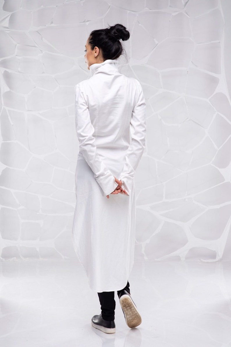 May include: A white long-sleeved shirt with a high collar and a long, flowing hem. The shirt is made of a lightweight fabric and has a relaxed fit.