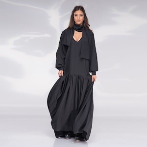 May include: A black maxi dress with a V-neckline and long sleeves. The dress has a gathered skirt and a scarf tied around the neck.
