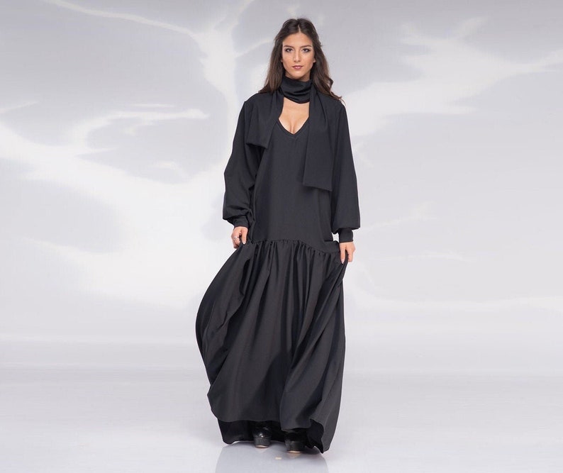 May include: A black maxi dress with a V-neckline and long sleeves. The dress has a gathered skirt and a scarf tied around the neck.