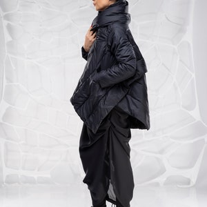 May include: A black puffer jacket with a high collar and a long, asymmetrical hem. The jacket is worn over black pants and black heeled sandals.