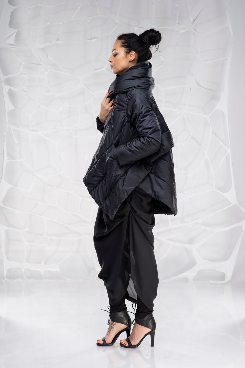 May include: A black puffer jacket with a high collar and a long, asymmetrical hem. The jacket is worn over black pants and black heeled sandals.