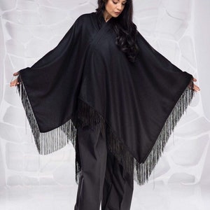 May include: A black poncho with fringe trim. The poncho is made of a soft, lightweight fabric and has a relaxed fit.