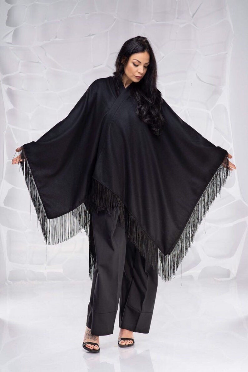 May include: A black poncho with fringe trim. The poncho is made of a soft, lightweight fabric and has a relaxed fit.
